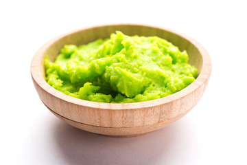 Green wasabi sauce or paste in bowl, with chopsticks or spoon over plain colourful background. selective focus
