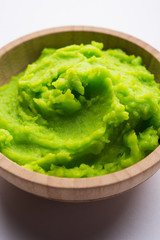 Green wasabi sauce or paste in bowl, with chopsticks or spoon over plain colourful background. selective focus