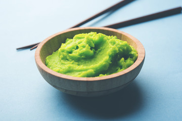 Green wasabi sauce or paste in bowl, with chopsticks or spoon over plain colourful background. selective focus