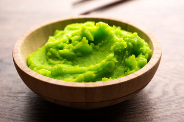Green wasabi sauce or paste in bowl, with chopsticks or spoon over plain colourful background. selective focus