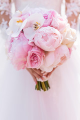 Bride in rich dress holds pink wedding bouquet of orchids and peonies