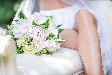 Obraz na płótnie Canvas White wedding bouquet lies by bride's knees