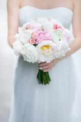Bride holds in her hands bouquet of white and pink peonies
