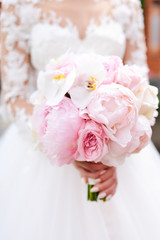 Bride in rich dress holds pink wedding bouquet of orchids and peonies