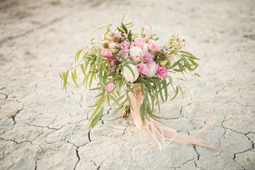 Rich wedding bouquet of pink flowers and greenery stands on the dry ground