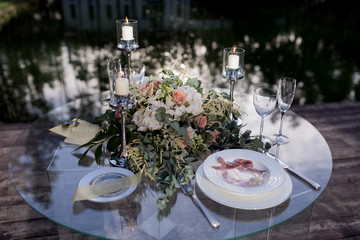 Glass table decorated for a romantic dinner stands on the bridge over the river