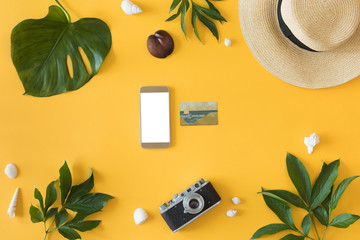 Flat lay on yellow background with mobile phone with white screen, palm leaf, vintage retro camera...
