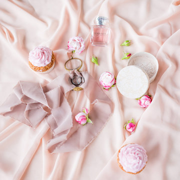 Silver wedding rings lie on the pink cloth among cakes and roses