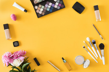 Makeup products with flowers and mobile phone on yellow background. Beauty background, flat lay, top view
