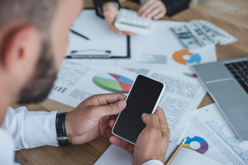 cropped image of financier using smartphone at table in office