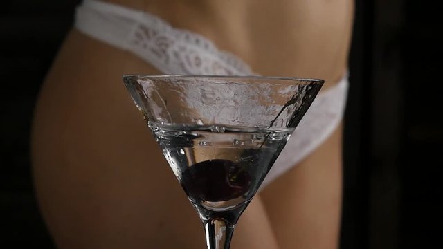 sexy young woman in a white panties prepares a cocktail with cherry in a dark. close-up buttocks and hip. slow motion
