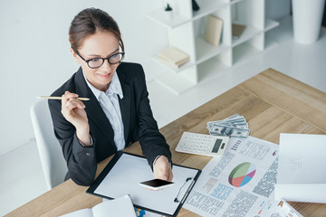high angle view of financier working at table in office and using smartphone