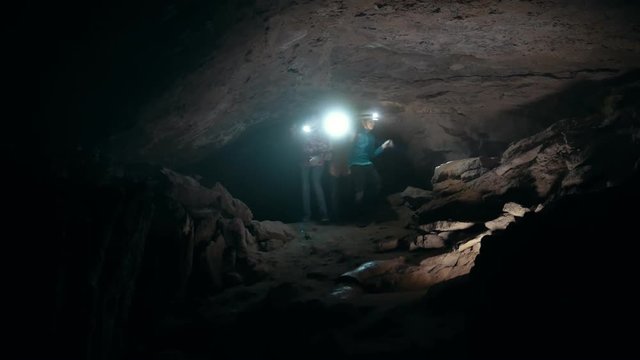 Group of teenagers with flashlights comes into a dark cave