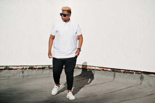 Stylish arabian muslim boy with originally hair and sunglasses posed on streets at roof against white wall.