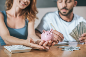 cropped image of couple planning family budget and holding piggy bank in living room