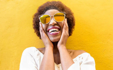 Fashion african woman smiling and wearing sunglasses with yellow ochre background