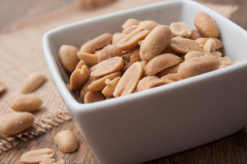 closeup of salted peanuts in a porcelain bowl on wooden background