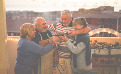 Senior friends having fun doing barbecue dinner in terrace outdoor - Mature people cheering with wine at bbq meal - Joyful elderly lifestyle, love and friendship concept