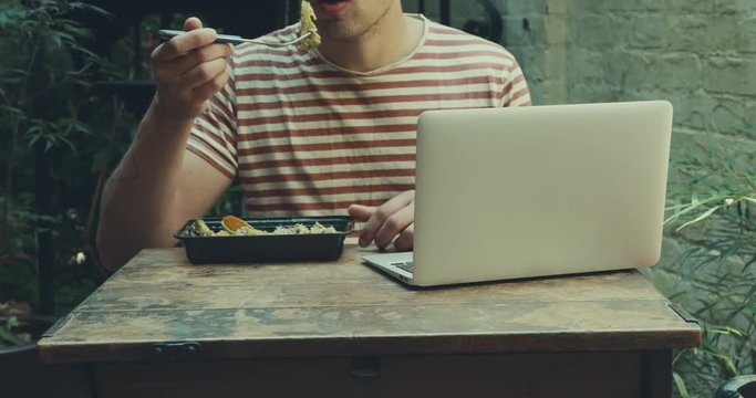 Man having lunch and using laptop computer in courtyard