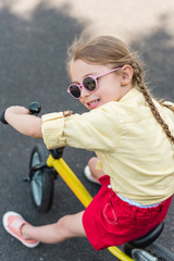 adorable smiling child in sunglasses riding bicycle