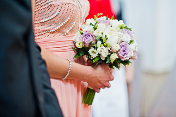Close-up photo of bridesmaid's hands holding wedding bouquet in the church.