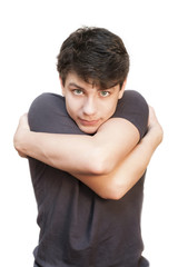 A beautiful teenager with dark hair and a sad face on a white background embraces himself. He misses the time when his parents and relatives often hugged him