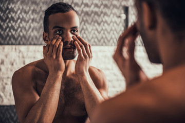 Afro-American Man Looking into Mirror in Bathroom.