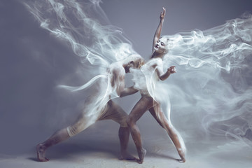 Dancing in flour. Naked couple in love in dust / fog. Girl and guy dancers wearing white sport clothing dancing in flour cloud on isolated background. Surreal concept.