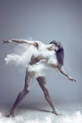 Dancing in flour concept. Naked muscle man dancer in dust / fog. Man wearing white shorts making dance element in flour cloud on isolated background
