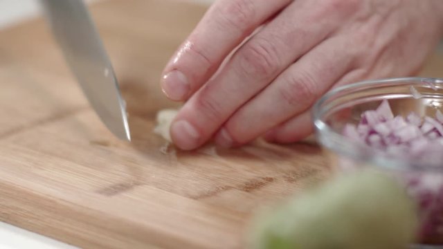 Chef mincing garlic clove with kitchen knife