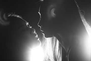 Silhouette of two sexy woman kissing holding in darkness through light and smoke