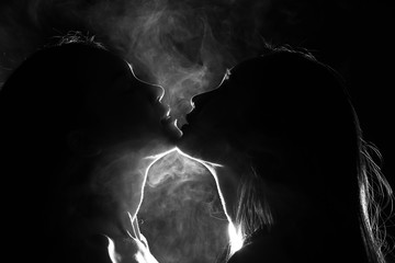 Silhouette of two sexy woman kissing holding in darkness through light and smoke - obrazy, fototapety, plakaty