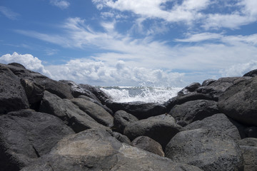 blue sunday sky day with waves splashing on shoreline rocks