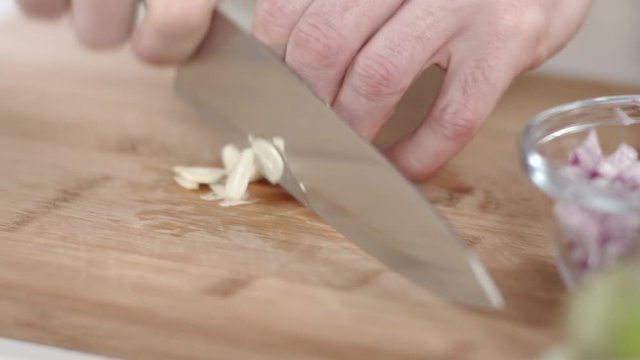 Slow-motion tracking shot of chef slicing garlic clove with kitchen knife