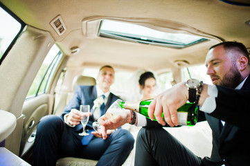 Groomsman opening the bottle and pouring champagni into glasses in the car.