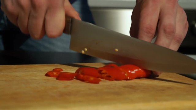 Slicing Red chili pepper. A man cuts pepper on a wooden Board
