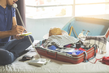 Young man hurring up to meeting and talking by phone and taking notes packing for Preparation travel suitcase at home