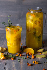 cocktail glass with orange juice, lemon, ginger, thyme and sea buckthorn on wooden background