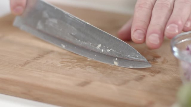 Slow-mo shot of chef mincing garlic clove with kitchen knife