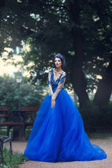 A mysterious sexy girl in a chic long blue dress in a gloomy park.