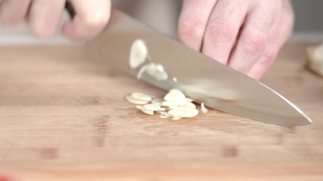 Slow-mo tracking shot of chef slicing and mincing garlic clove with kitchen knife