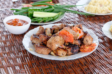 On the wicker table plates with pieces of shish kebab, porridge and vegetables. Summer dinner in the open air. Closeup view.