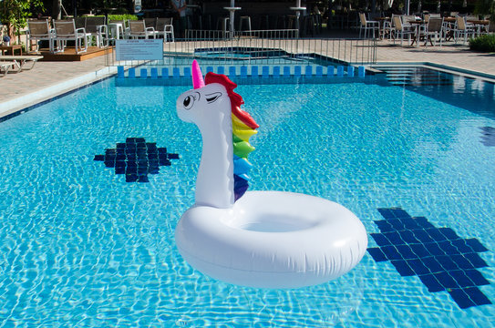 Unicorn pool float in blue water background, inflatable swim tube. Pool party, summer holidays, beach vacation. Unicorn inflatable float for kids and adult.