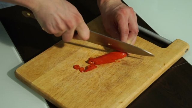Slicing Red chili pepper. A man cuts pepper on a wooden Board