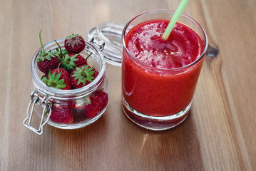 Healthy homemade strawberry smoothies in a glass with a straw for a cocktail and strawberries in a glass jar on a wooden board