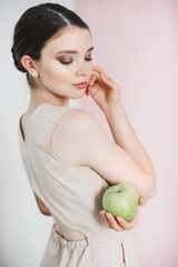 A young woman is standing and holding a big green apple in her hand.