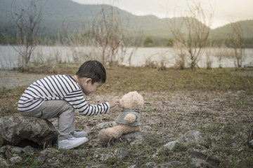 child asian with teddy bear sitting site the reservoir is the background.