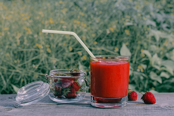 Healthy homemade strawberry smoothies in a glass with a straw for a cocktail and strawberries in a glass jar on a wooden board