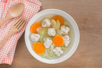 top view of pork ball clear soup with chinese cabbage and carrot in a ceramic bowl on wooden table. asian homemade style healthy food concept.
