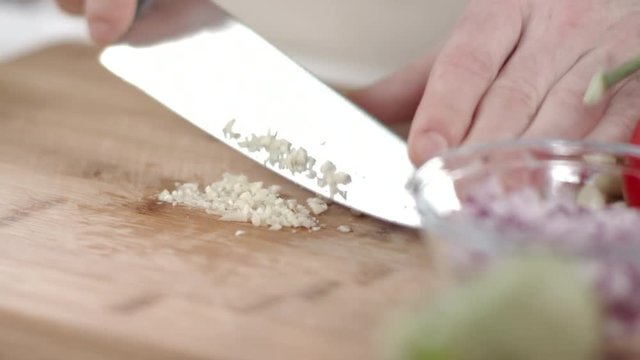 Slow-mo shot of chef mincing garlic clove with kitchen knife